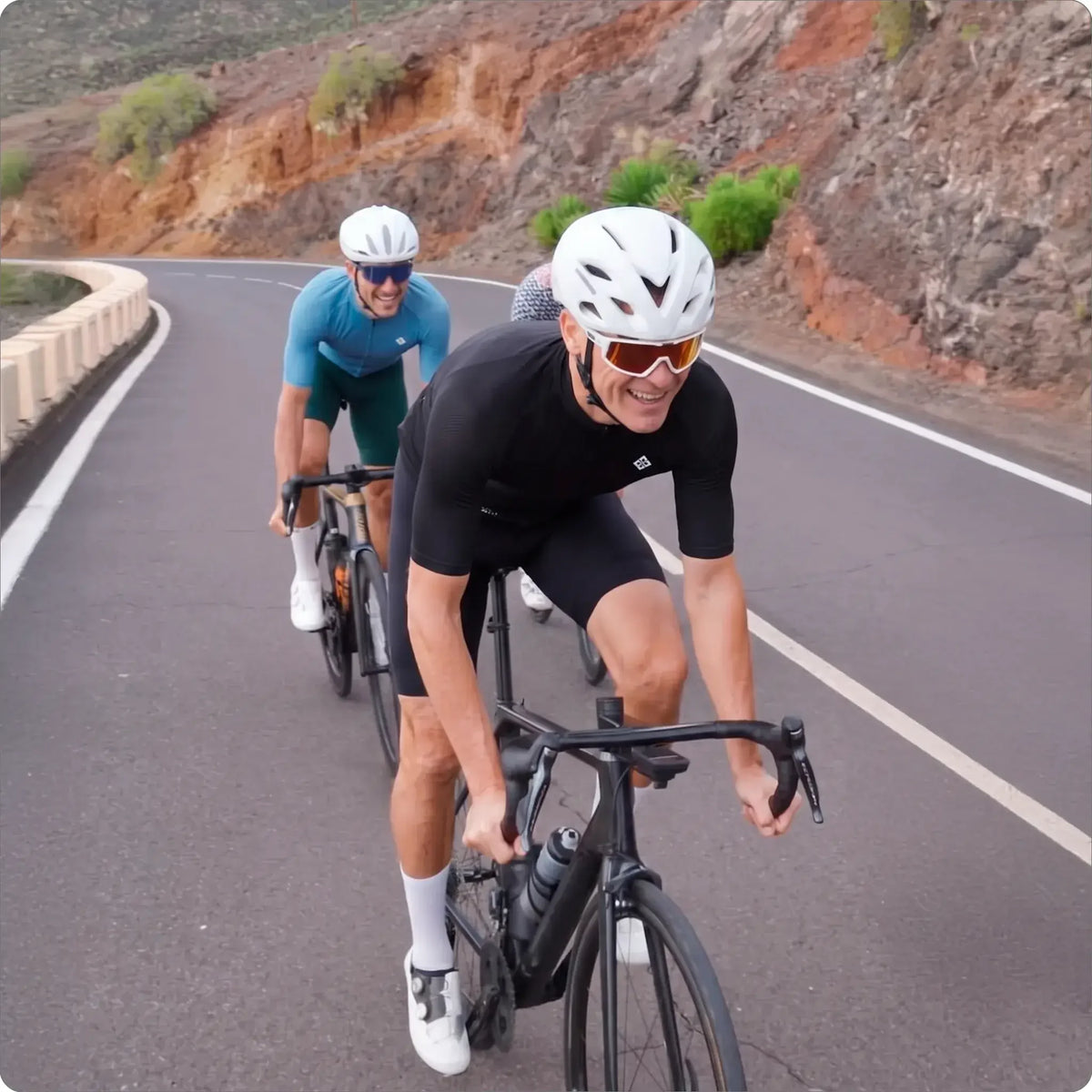 Cyclists riding road bikes on a scenic mountain road, wearing helmets and sportswear