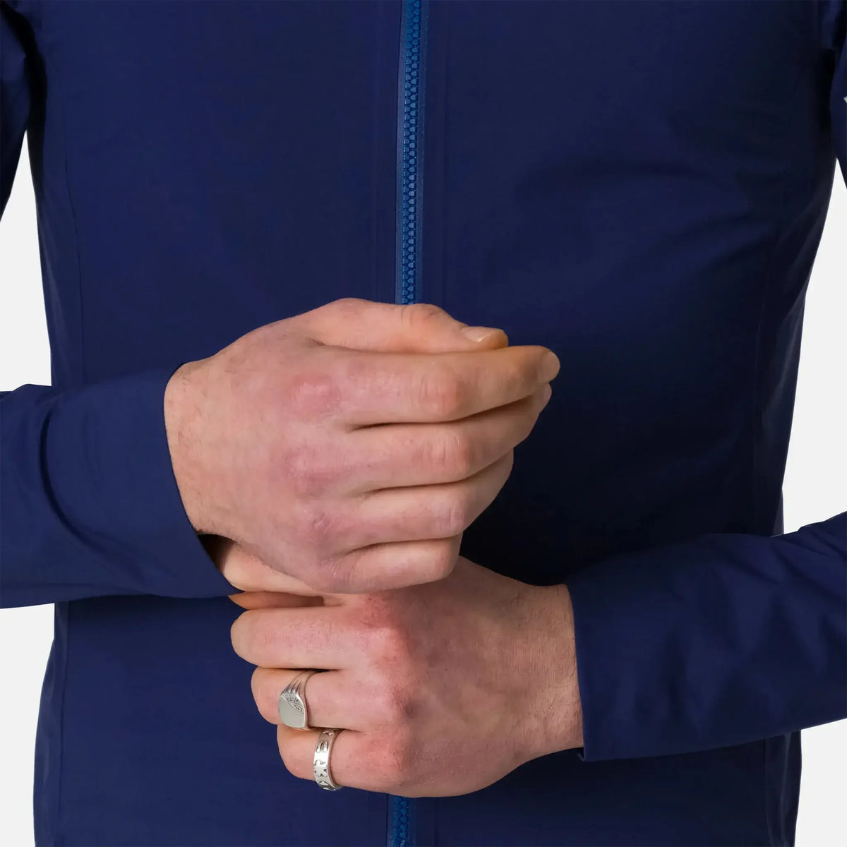 Man wearing navy blue zip-up jacket with hands clasped, showcasing silver rings on fingers