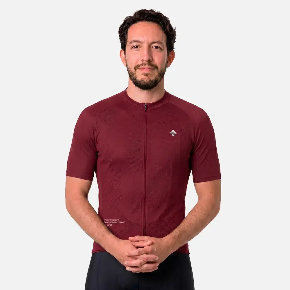 Man wearing maroon cycling jersey with front zipper and logo, paired with black shorts